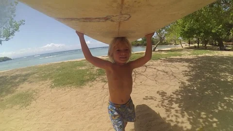 Cute boy walking on ocean beach holding surfboard on his head. POV Stock Footage 74983460