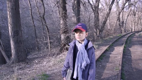 Cute boy walking on railway in forest with a book in his hand 库存影片 172585070