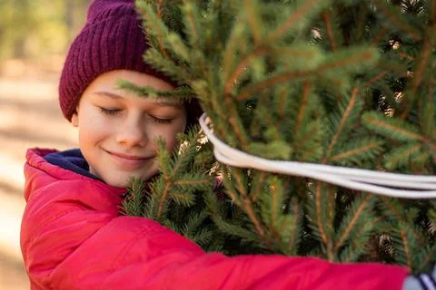 Cute boy in a warm red hat and jacket hugging a christmas tree Stock Photos