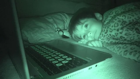 Cute boy watches notebook in bed at night Stock Footage 100097940