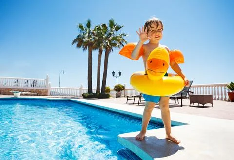 Cute boy waving hands standing on the edge of swimming pool Stock Photos