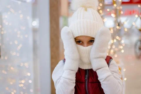 Cute boy in white bobble hat and scarf at mall near showcase. blurred bright Stock-Fotos