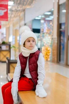 Cute boy in a white fluffy hat in a shopping center against the background of Stock Photos