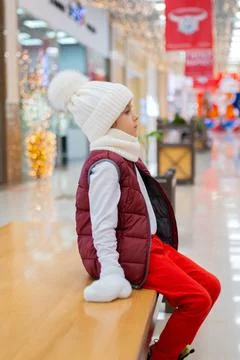 Cute boy in a white fluffy hat in a shopping center against the background of Stock Photos