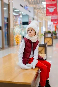 Cute boy in a white fluffy hat in a shopping center against the background of Stock Photos