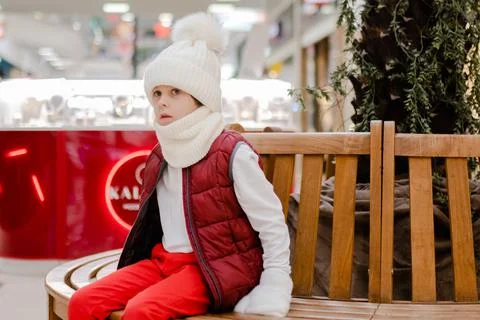 Cute boy in a white fluffy hat in a shopping center and pointing something up Stock Photos