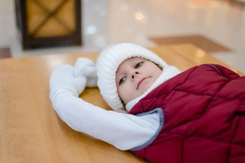 Cute boy in a white fluffy hat in a shopping center against the background of Stock Photos