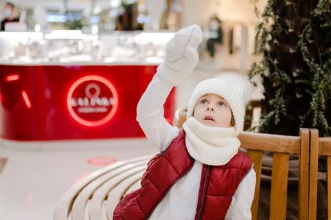Cute boy in a white fluffy hat in a shopping center and pointing something up Stock Photos