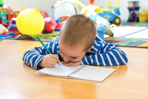Cute boy writing something in notebook on the floor Stock Photos