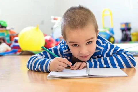 Cute boy writing something in notebook on the floor Stock Photos