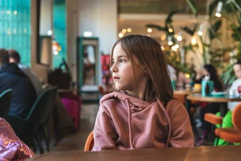 A cute brooding girl sits at a table in a cafe and looks out the window Stock Photos