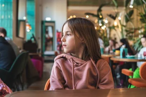 A cute brooding girl sits at a table in a cafe and looks out the window Stock Photos