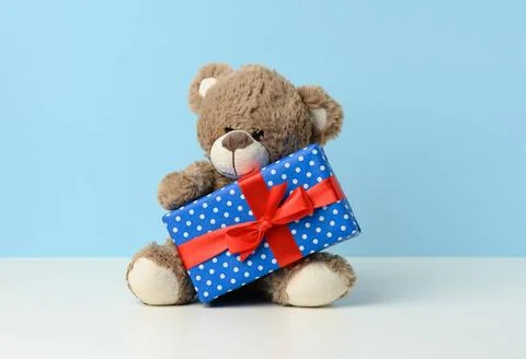 Cute brown teddy bear holding a box wrapped in blue paper and red silk rib... Stock Photos