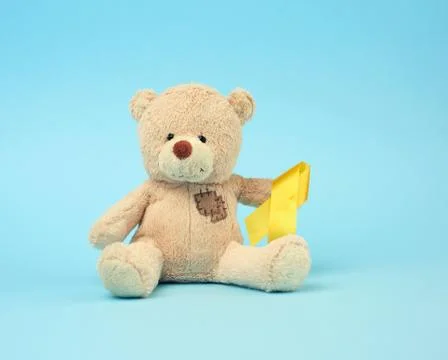 Cute brown teddy bear with a patch holds a silk yellow ribbon in the shape of Stock Photos