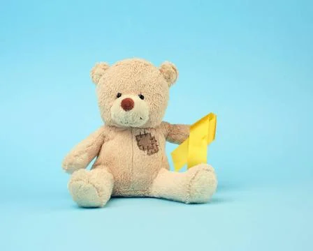 Cute brown teddy bear with a patch holds a silk yellow ribbon in the shape... Stock Photos