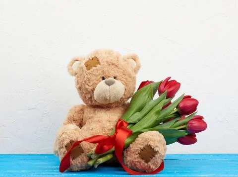Cute brown teddy bear with patches sits on a blue wooden background and ho... Foto stock