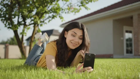 Cute brunette communicating through video call on phone lying on green lawn Stock Footage 244380966