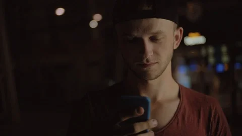 Cute Caucasian guy in black cap looking at screen of smartphone, smiling. Young Stock Footage 91155202