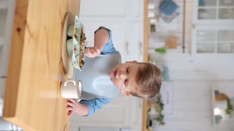 Cute caucasian toddler boy eats vegetables and meat on his own using a fork Stock Footage 234396157