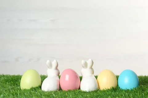 Cute ceramic Easter bunnies and dyed eggs on green grass. Space for text Foto stock