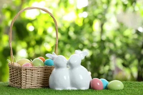 Cute ceramic Easter bunnies with wicker basket and dyed eggs on green grass a Foto stock