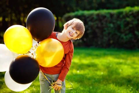 Cute charming red-haired boy with colorful balloons in an open park. The kid  Foto stock