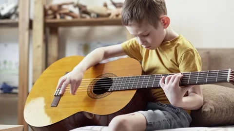 A cute cheerful boy is playing classical guitar in the children's room. Stock Footage 277942796