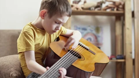 A cute cheerful boy is playing classical guitar in the children's room. Stock Footage 277942818