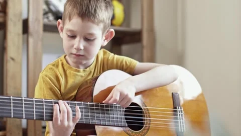 A cute cheerful boy is playing classical guitar in the children's room. Stock Footage 277942851