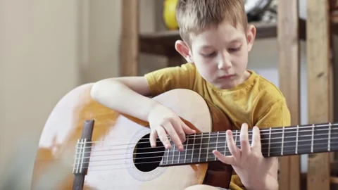 A cute cheerful boy is playing classical guitar in the children's room. Stock Footage 277942882