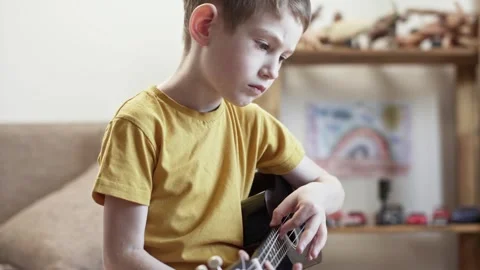 A cute cheerful boy is playing the ukulele in the children's room Stock Footage 277942710