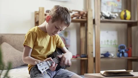 A cute cheerful boy is playing the ukulele in the children's room Stock Footage 277942737