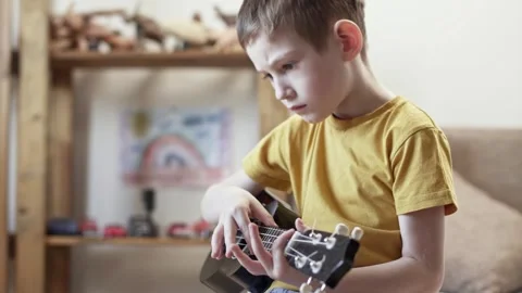 A cute cheerful boy is playing the ukulele in the children's room Stock Footage 277942738