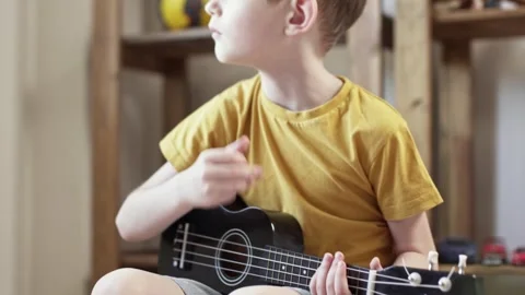 A cute cheerful boy is playing the ukulele in the children's room Stock Footage 277942891