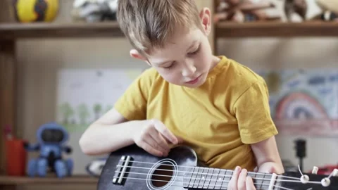 A cute cheerful boy is playing the ukulele in the children's room Stock Footage 277942919