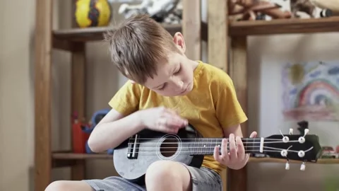 A cute cheerful boy is playing the ukulele in the children's room Stock Footage 277942924