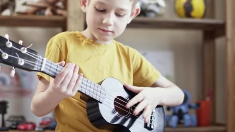 A cute cheerful boy is playing the ukulele in the children's room Stock Footage 277942936