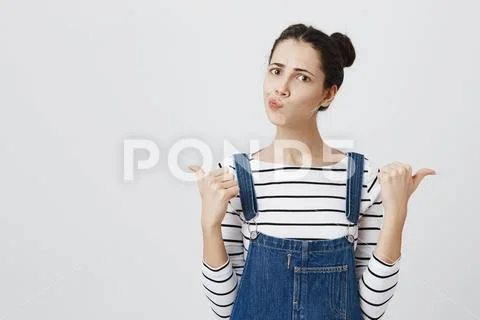 Cute cheerful brunette girl pouting lips and pointing fingers away, frowning Stock Photos