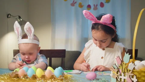 Cute cheerful children in Easter bunny costumes color eggs at home at the table Stock Footage 258395671