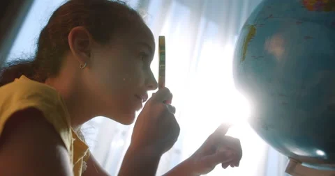Cute Child 9 years old looks at globe through magnifying glass,technology for Vidéo 239482771