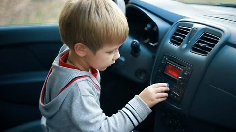 Cute child boy kid playing in the vehicle interior, turns on the car radio Stock Footage 101061871
