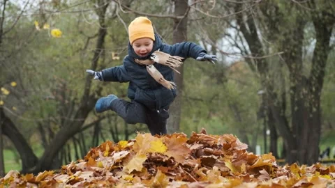 Cute child boy running and jumping into pile of autumn leaves in city park. Stock Footage 171413548