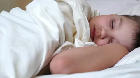 Cute child boy wakes up in cozy white bed lying on pillow. young baby kid sle Stock Footage 136031442