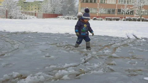 Cute child breaking ice layer of big frozen puddle with boots Video stock 96523543