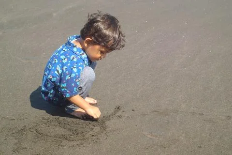 Cute child drawing picture on a sand playing outdoor on summer beach. Boy d.. Stock Photos