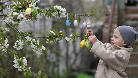 A cute child hangs colorful easter eggs on a flowering tree. against the Stock Footage 184606804