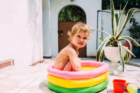 Cute child has fun in inflatable pool with toys in summer in backyard. Photos