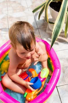 Cute child has fun in inflatable pool with toys in summer in backyard. Stock Photos