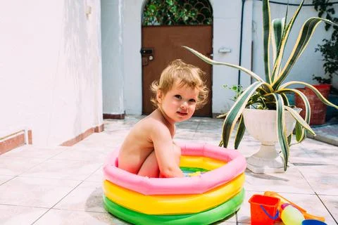 Cute child has fun in inflatable pool with toys in summer in backyard. Фото