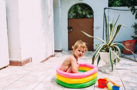 Cute child has fun in inflatable pool with toys in summer in backyard. Фото